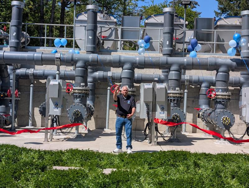 Man stands in front of a large seawater system, cutting red ribbon during a ceremony to celebrate the new upgrade to the system.